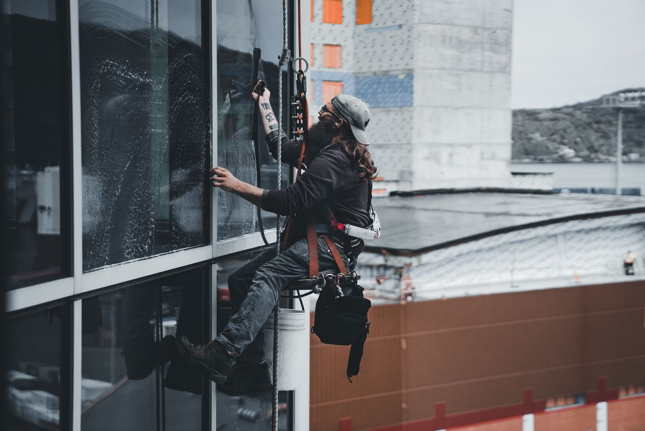 A man washing the windows of a skyscraper while secured in a harness, highlighting work performed on tall urban buildings.
